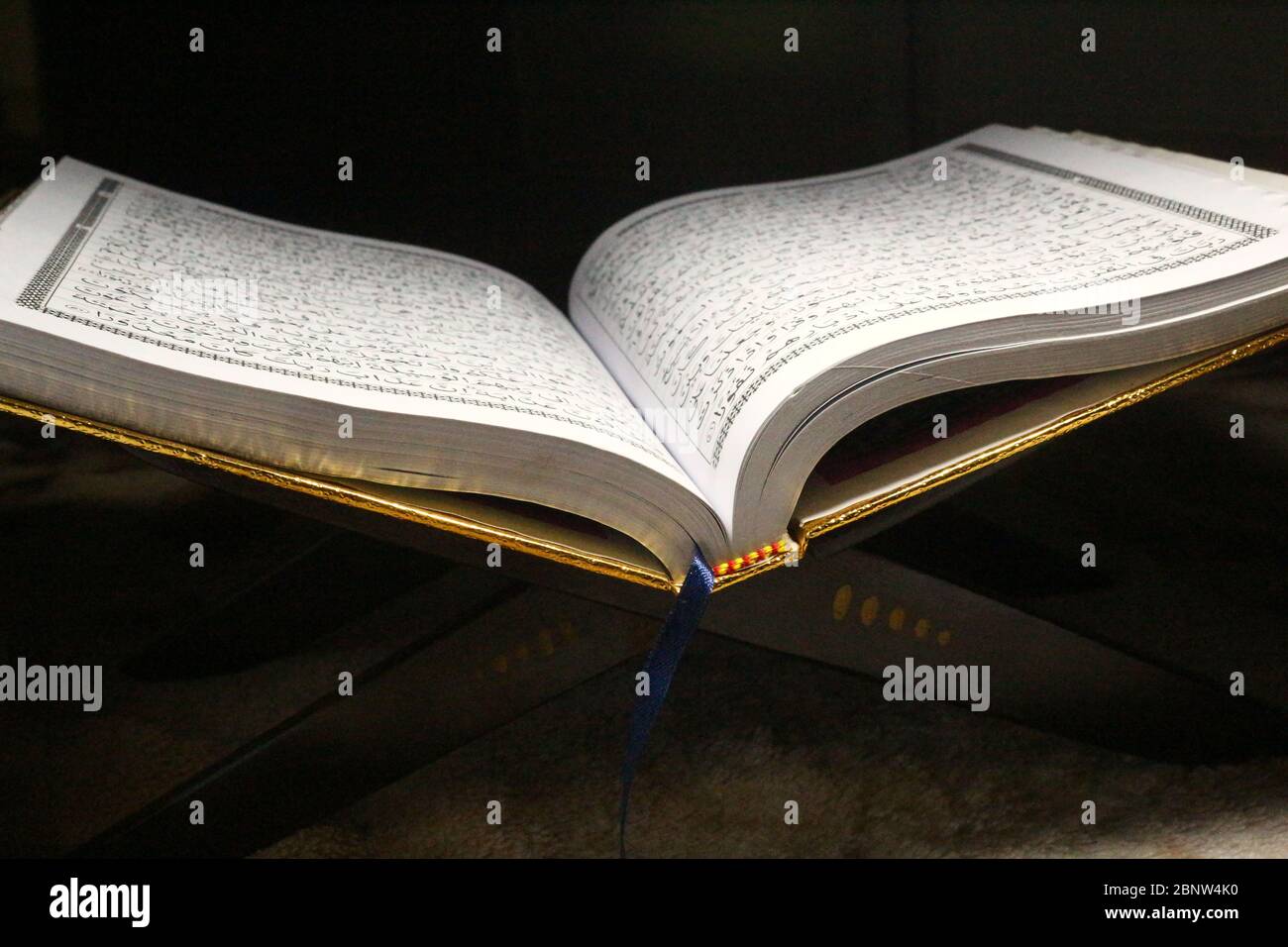 Livre du Coran sur un tapis marron, ouvert et isolé sur fond sombre Banque D'Images