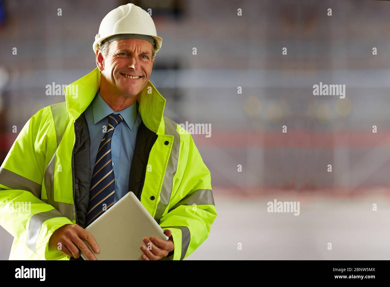 Portrait d'un architecte mûr souriant portant un casque et des vêtements réfléchissants tenant une tablette numérique sur le chantier Banque D'Images