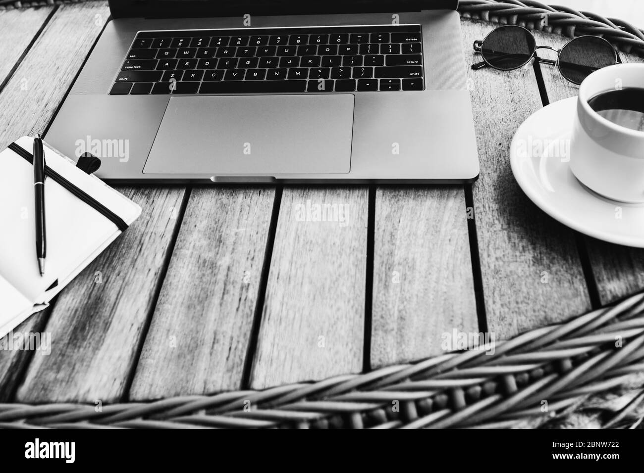 Photo en noir et blanc d'un espace de travail avec ordinateur portable, sur une table en bois avec une tasse de café et un carnet pour enregistrer les étuis. Commande à distance Banque D'Images