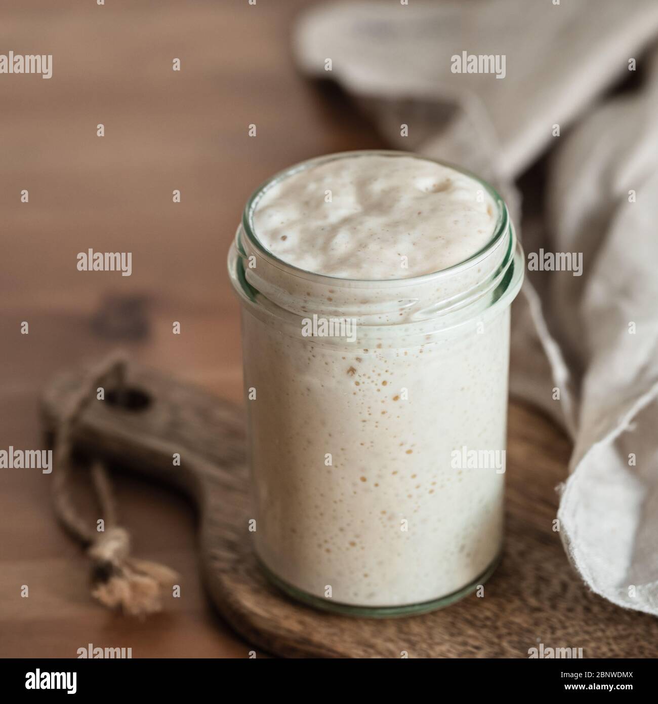 Démarreur de levain de blé. Bol en verre avec base de levain sur planche à découper en bois sur table en bois. Copier l'espace pour le texte ou la conception. Banque D'Images