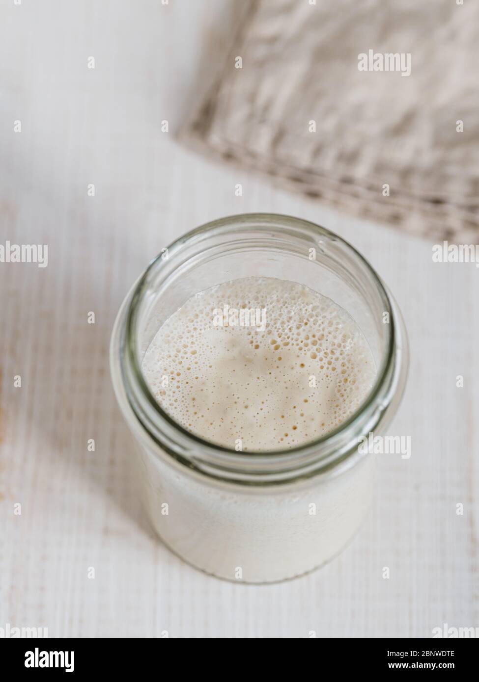 Démarreur de levain de blé. Vue de dessus du bol en verre avec démarreur de levain sur fond de bois blanc. Copier l'espace pour le texte ou la conception. Verticale. Banque D'Images