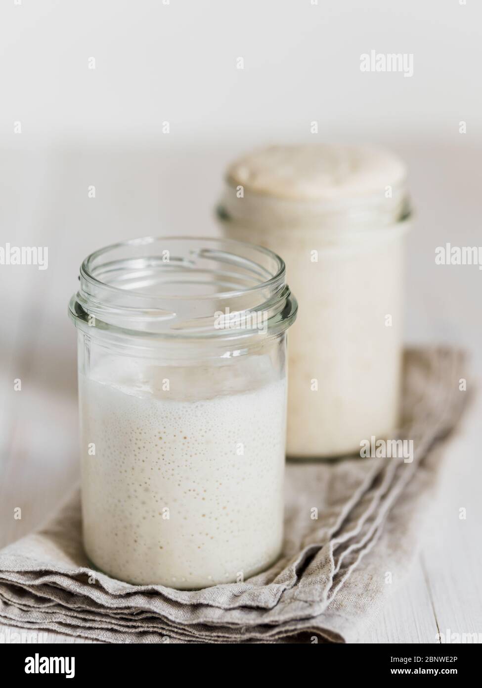 Deux pots en verre avec des démarreurs de levain de blé dans différents niveaux d'hydratation. Starter 100% hydratation en arrière-plan et Starter avec une hydratation plus élevée en premier plan. Copier l'espace. Verticale. Banque D'Images