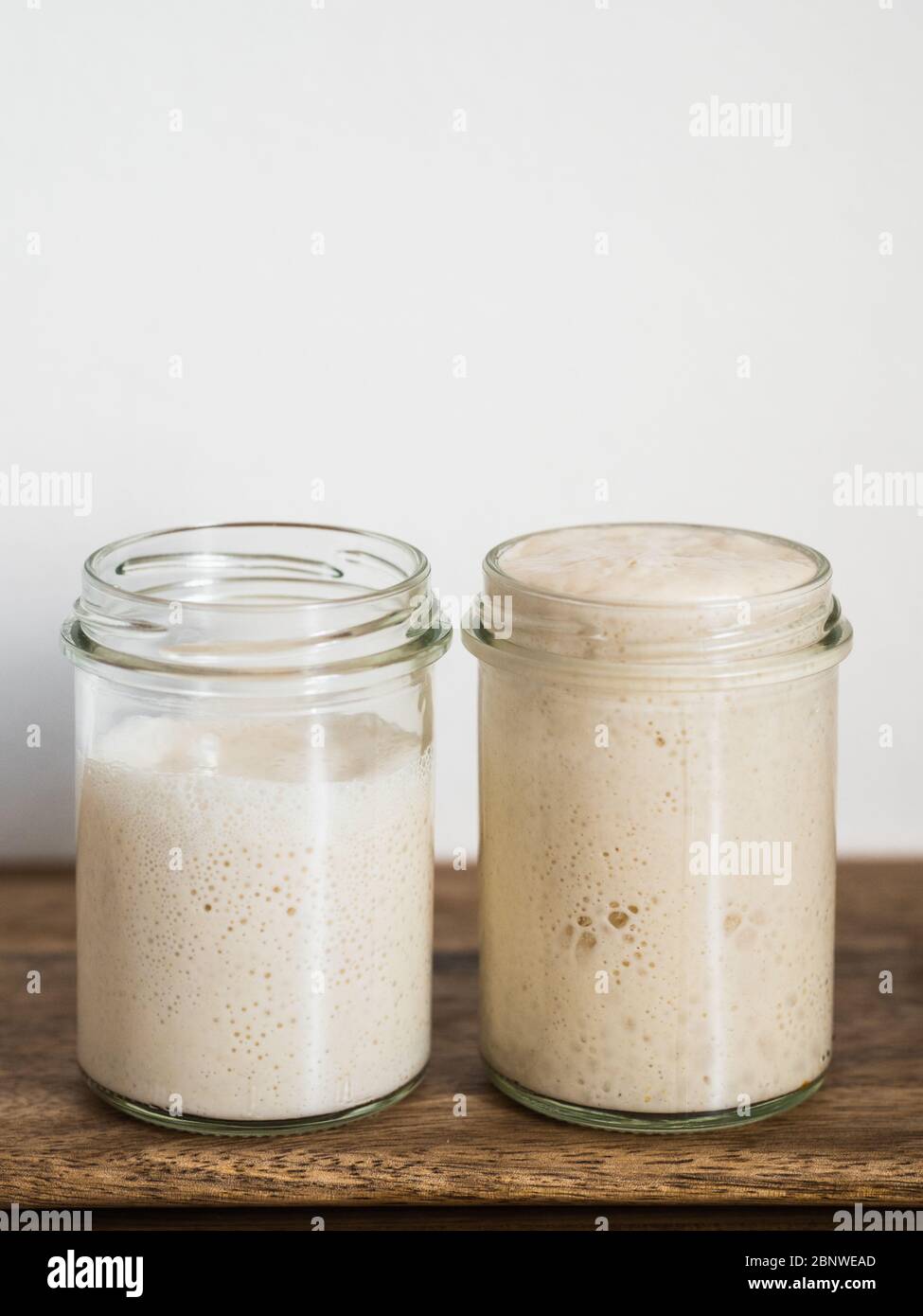 Deux pots en verre avec des démarreurs de levain de blé dans différents niveaux d'hydratation. Starter 100 % d'hydratation (droite) et Starter avec une hydratation plus élevée (gauche). Copier l'espace haut. Verticale. Banque D'Images