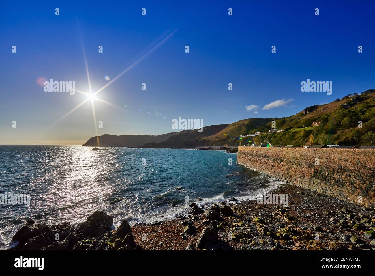 Image de la mer et du promontoire de bonne nuit Bay, derrière le mur du port au lever du soleil avec un ciel bleu clair, les îles du canal de Jersey Banque D'Images