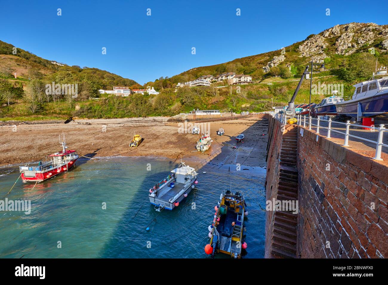 Image de la baie de bonne nuit et du port à marée basse avec des rochers, des galets et des chanis d'amarrage, ciel bleu et soleil brillent, tôt le matin, Jersey ci Banque D'Images