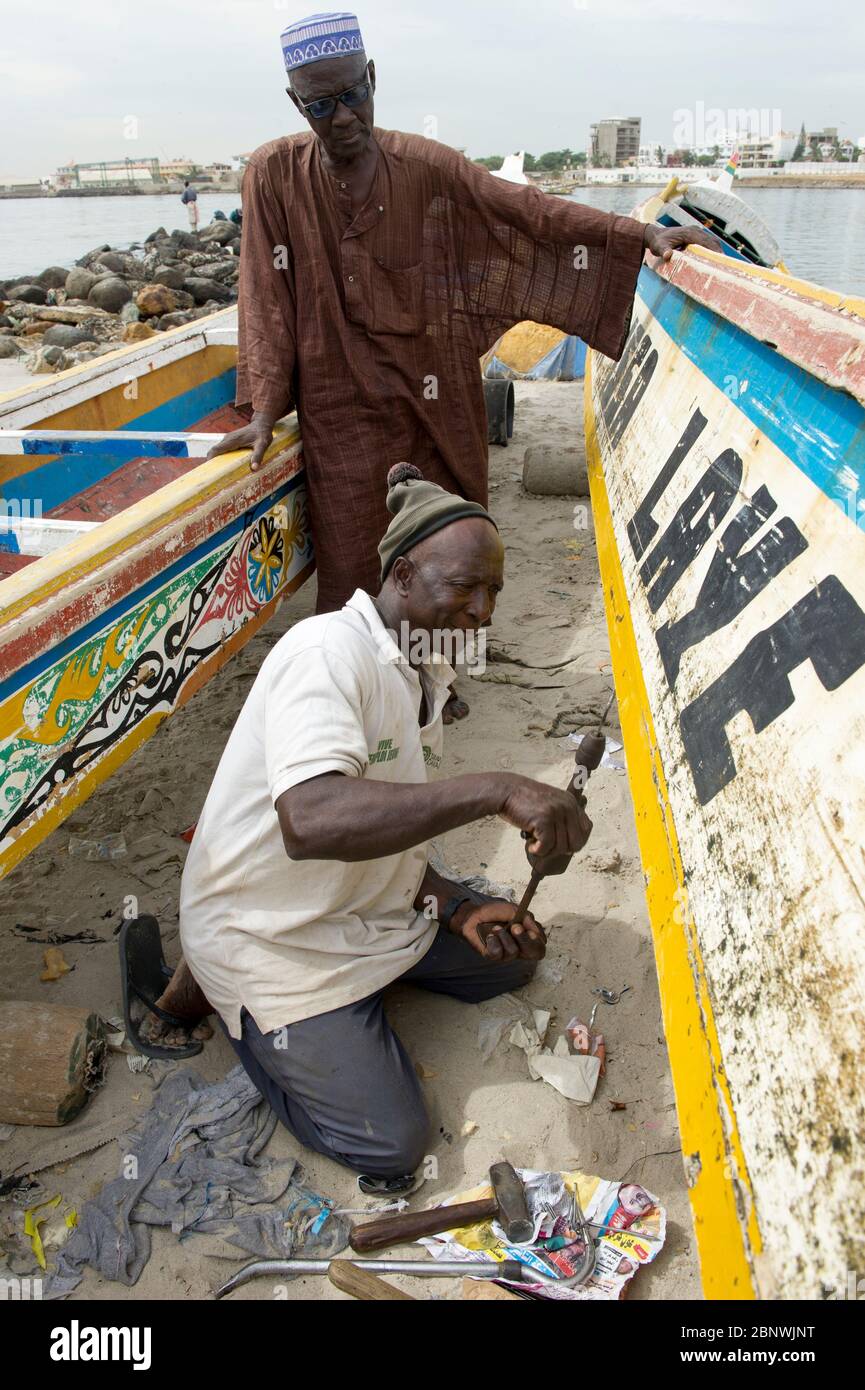 Hommes réparant un bateau de pêche traditionnel Pirogue sur la plage de Soumbedioune, Dakar, Sénégal. Banque D'Images