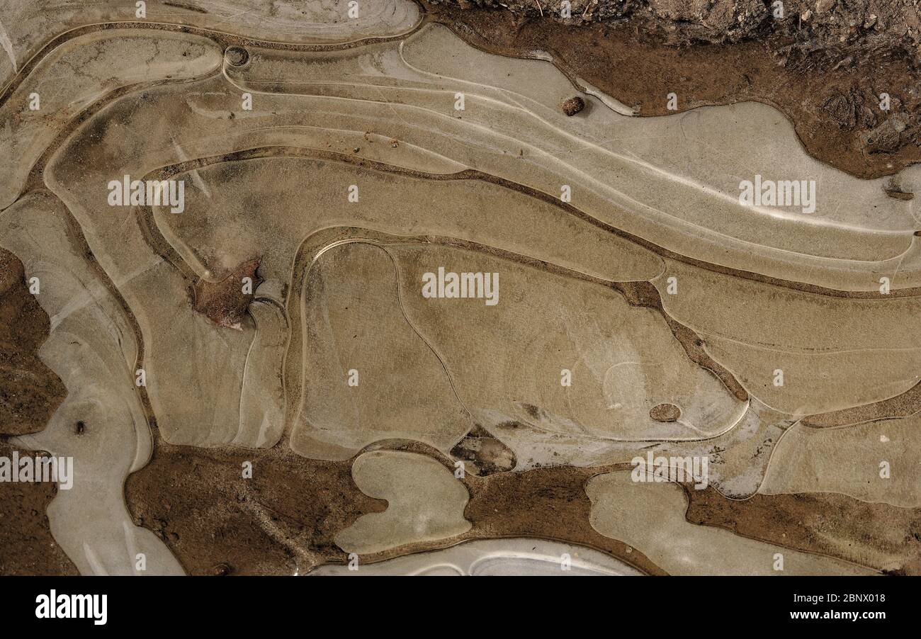 Vue de dessus gros plan de l'eau transformée en glace pendant la nuit sur une route de terre boueuse créant des motifs et textures naturels abstraits tout au long. Apparence Banque D'Images