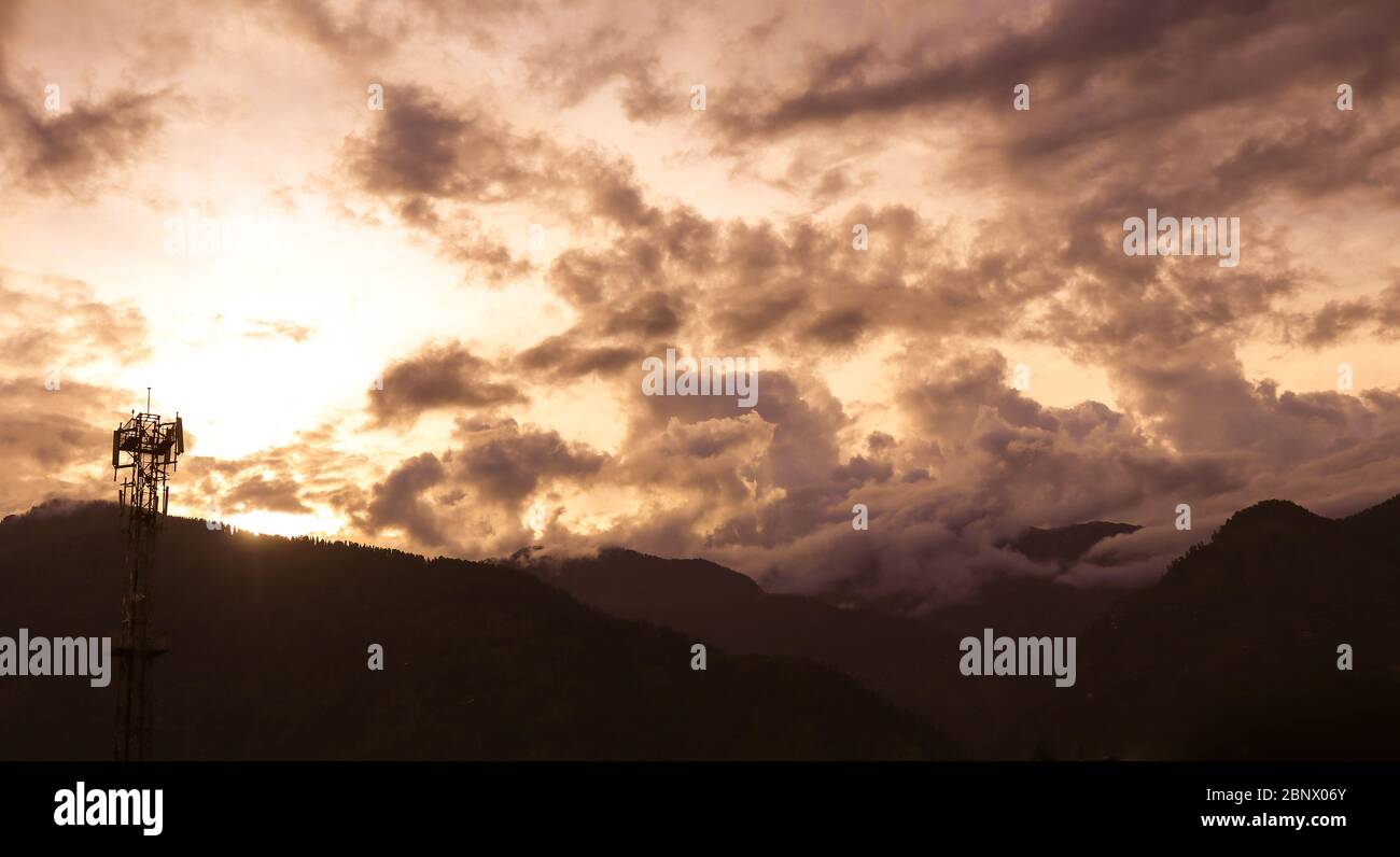 Silhouette Paysage d'une tour de communication et de nuages spectaculaires qui couvrent les montagnes au coucher du soleil. Banque D'Images