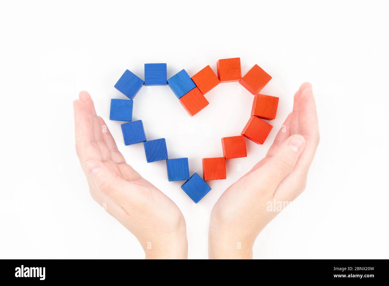 Vue rognée des mains de femmes près d'un arrangement en forme de coeur de petits blocs de bois rouges et bleus sur fond blanc, vue de dessus. Soins, soutien, charité Banque D'Images