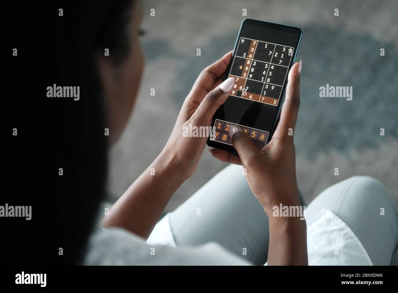 Femme noire jouant Sudoku au téléphone pour l'entraînement de cerveau Banque D'Images