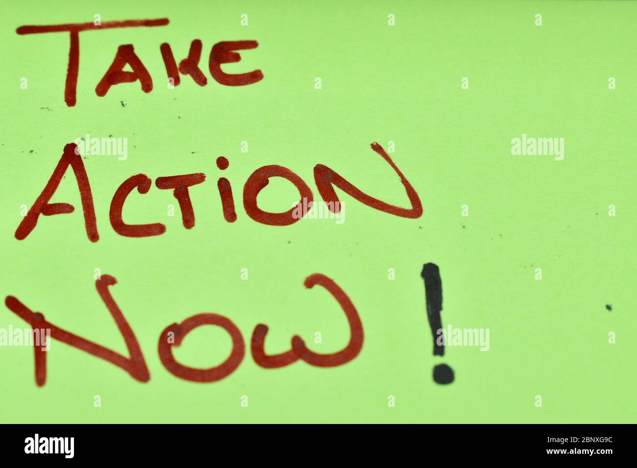 Gros plan d'une note post-it de couleur vert fluorescent.les mots « prendre l'action maintenant » sont écrits à la main sur des majuscules dans un marqueur rouge. Banque D'Images