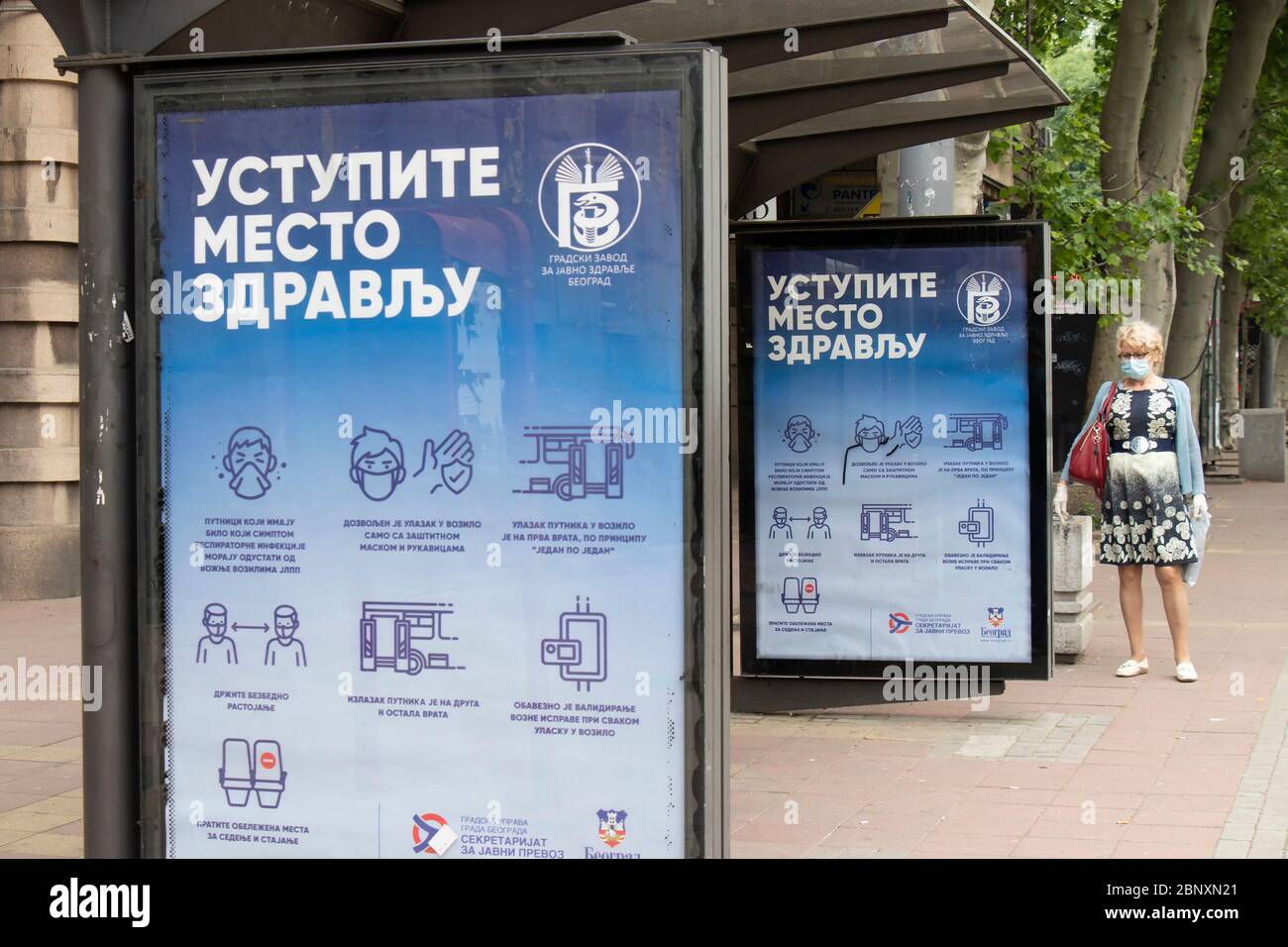 Belgrade, Serbie - 15 mai 2020 : une femme blonde mature portant un masque chirurgical et des gants debout seule à l'arrêt d'autobus avec des directives sur le coronavirus Banque D'Images