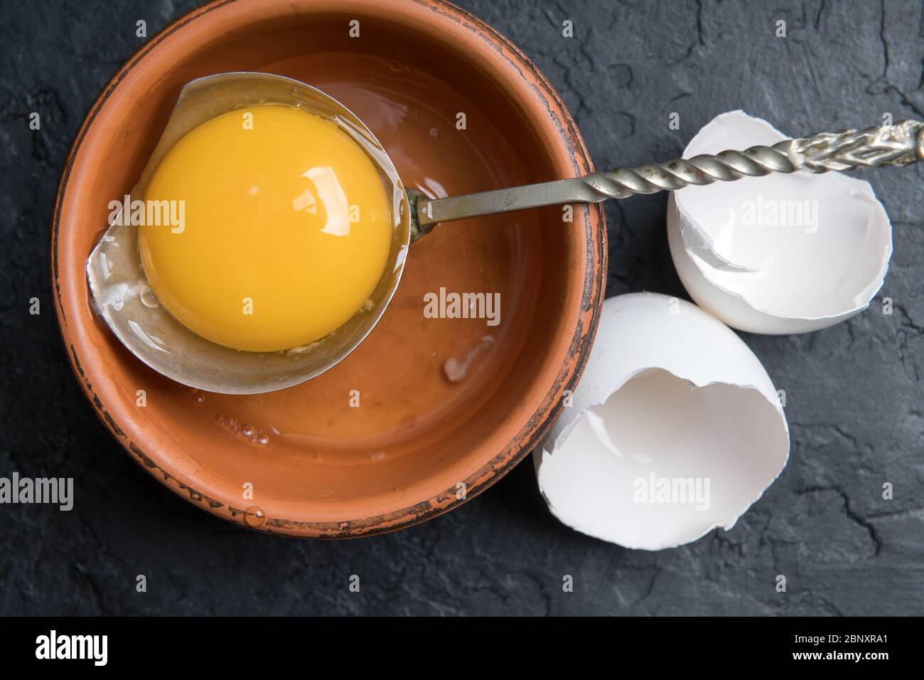 Jaune de poulet provenant d'œufs biologiques cassés dans une plaque brune sur fond de béton noir. Photographie alimentaire Banque D'Images