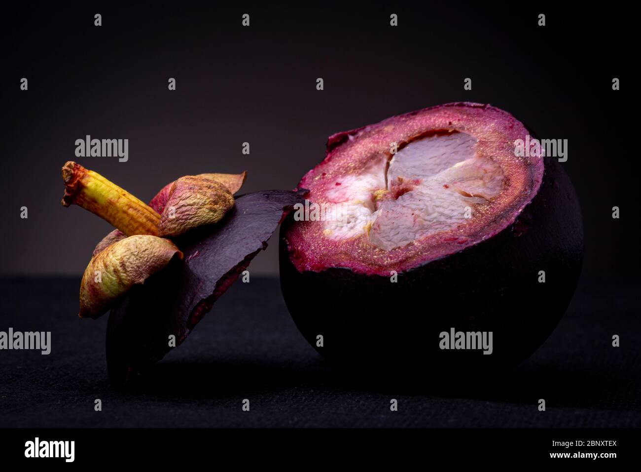 Tige colorée et dessus reposant en plus du fruit Mangosteen exotique rouge-violacé montrant sa chair blanche interne et son épais zeste rouge spongieux. Banque D'Images