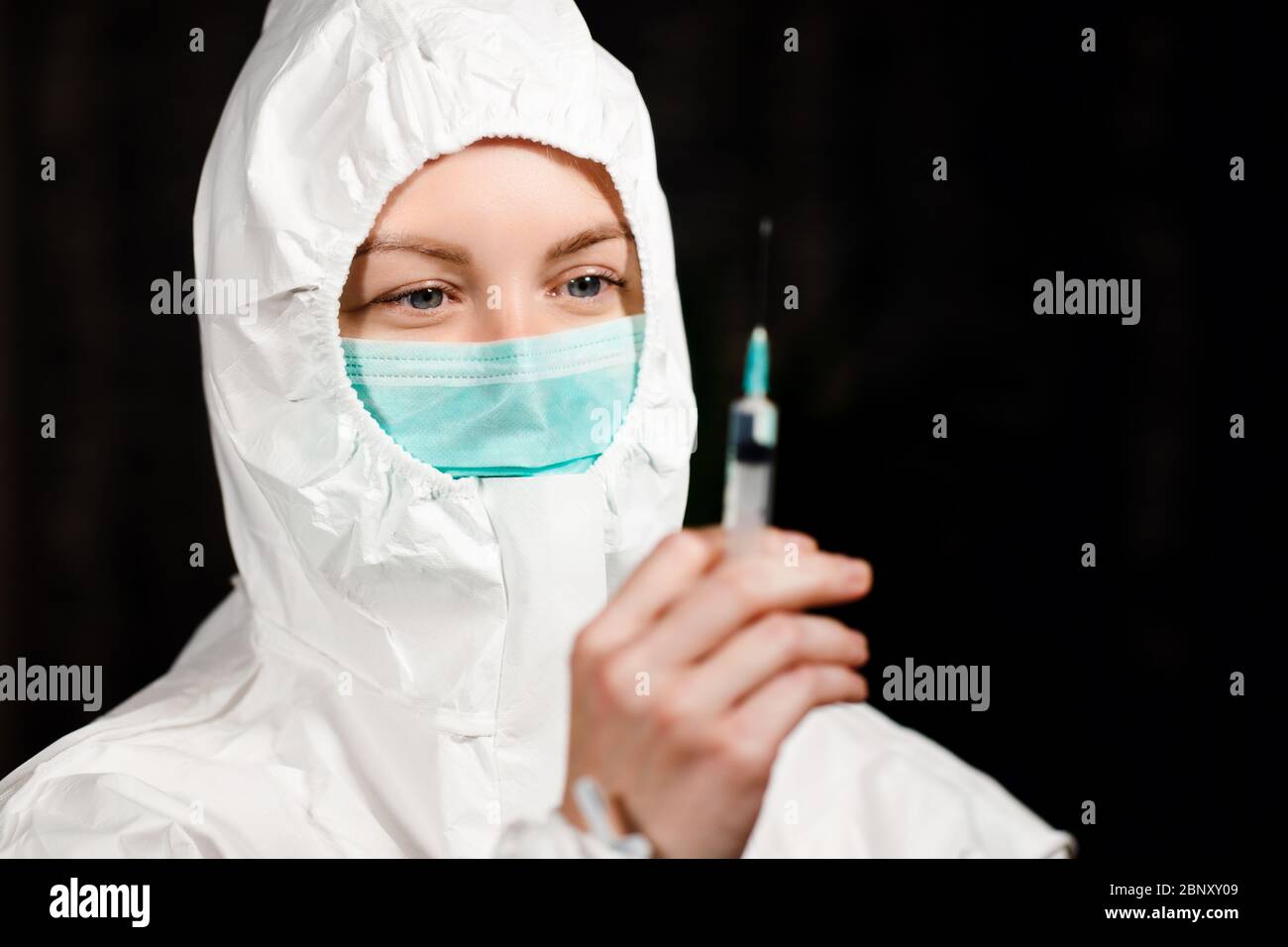 Médecin en costume médical de protection et masque chirurgical regarde la seringue Banque D'Images