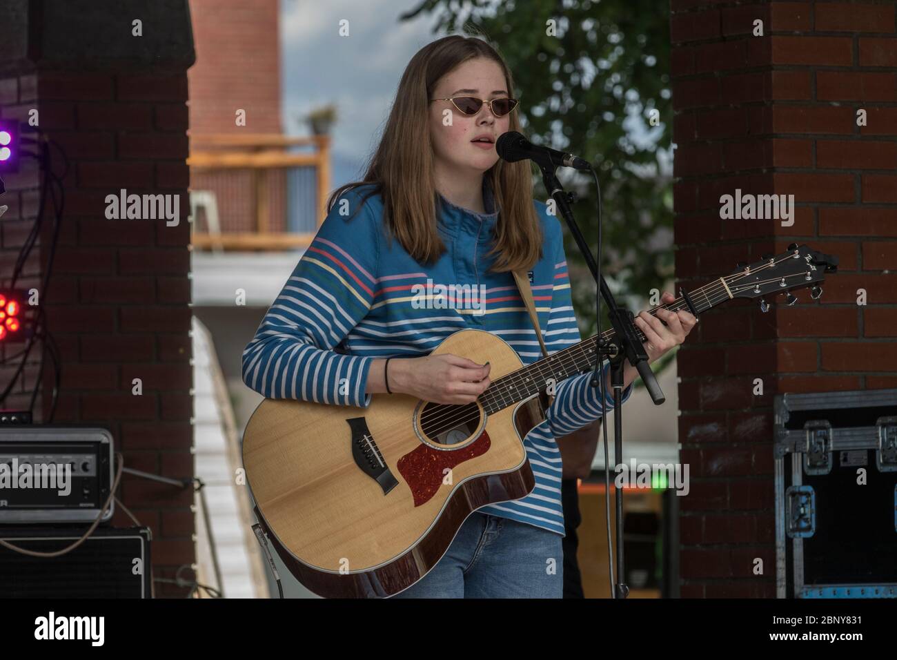 Une jeune fille à cheveux longs, avec des lunettes de soleil fraîches, jouant de la guitare et chantant dans un groupe, au concert de l'extérieur Banque D'Images