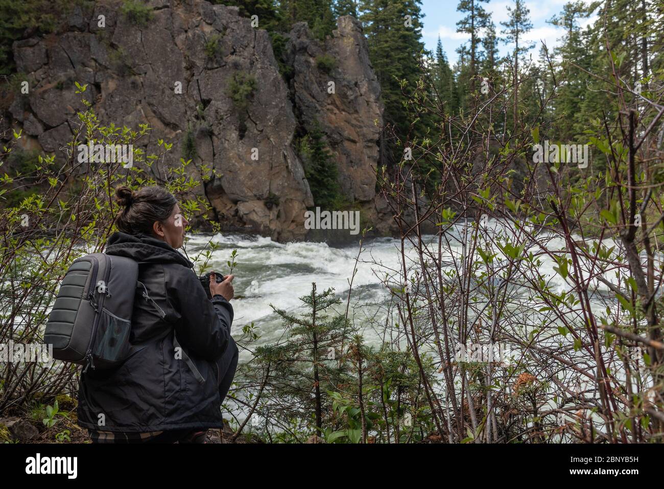 Femme d'âge moyen, portant un sac à dos gris et un appareil photo à la main, se préparer à photographier une rivière qui se précipite Banque D'Images