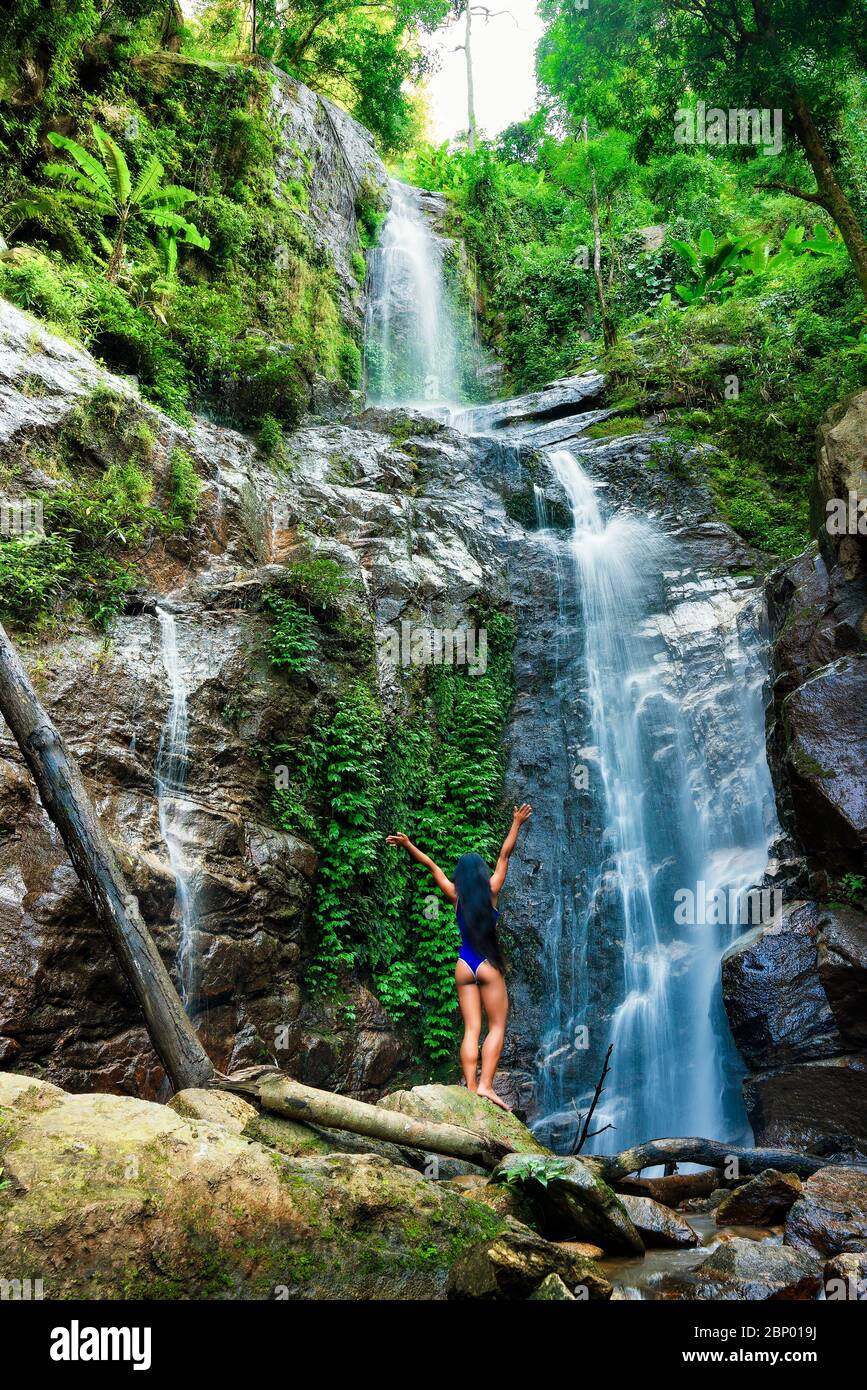 Vue arrière du jeune femme debout devant une chute d'eau avec ses mains posées. Touristiques femelle avec ses bras tendus à la recherche à cascade. Banque D'Images