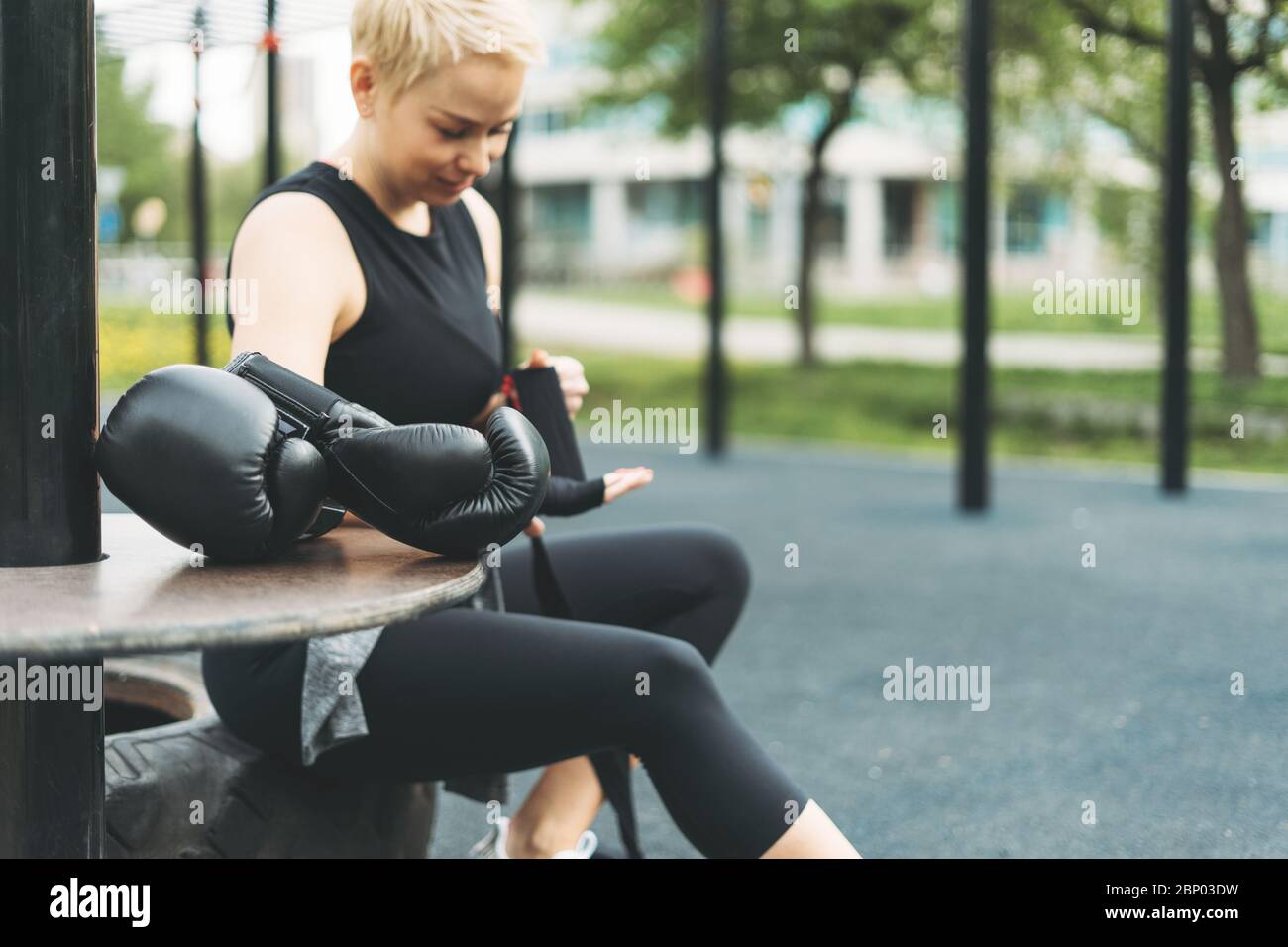 Gants de boxe en cuir noir sur le fond de la jeune fille athlétique secoue les bandages de boxe sur les mains avant l'entraînement Banque D'Images