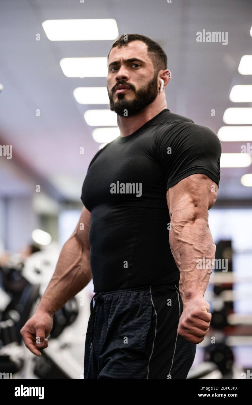 jeune homme à barbe forte en vêtements de sport noirs montrant sa séparation musculaire et veineuse sur les triceps après l'entraînement en salle de sport Banque D'Images