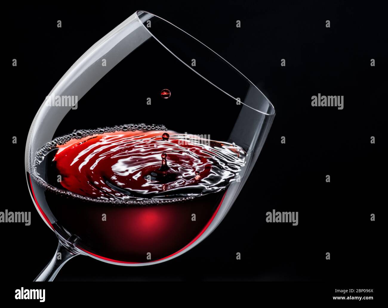 Vin rouge dans un verre de vin isolé sur un fond noir. Chute à la surface et crée des courbes. Banque D'Images