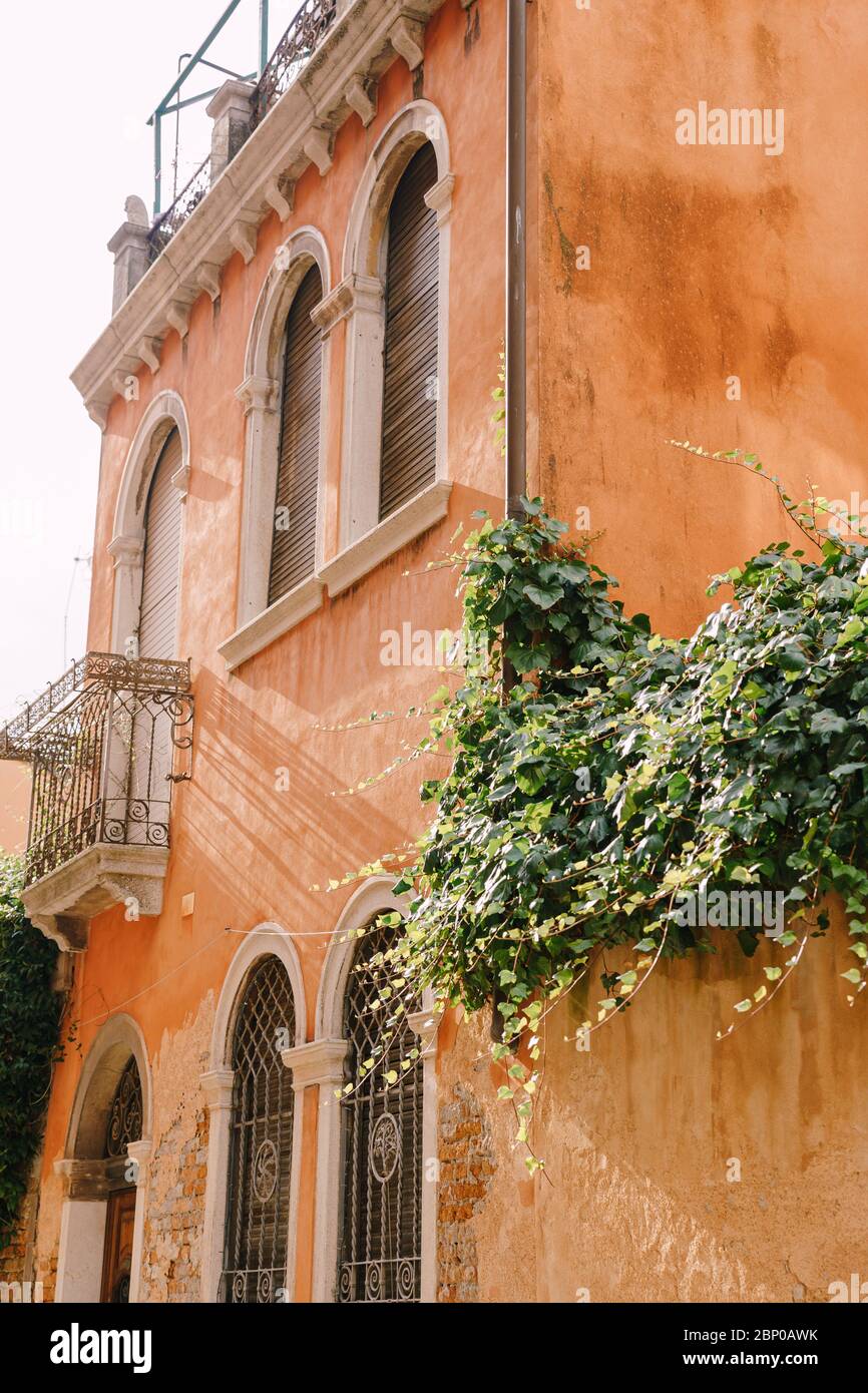 Ancien bâtiment à Venise, Italie, gros plan. Murs couleur pêche, fenêtres en arches vénitiennes classiques avec volets en bois, petit balcon avec forge Banque D'Images