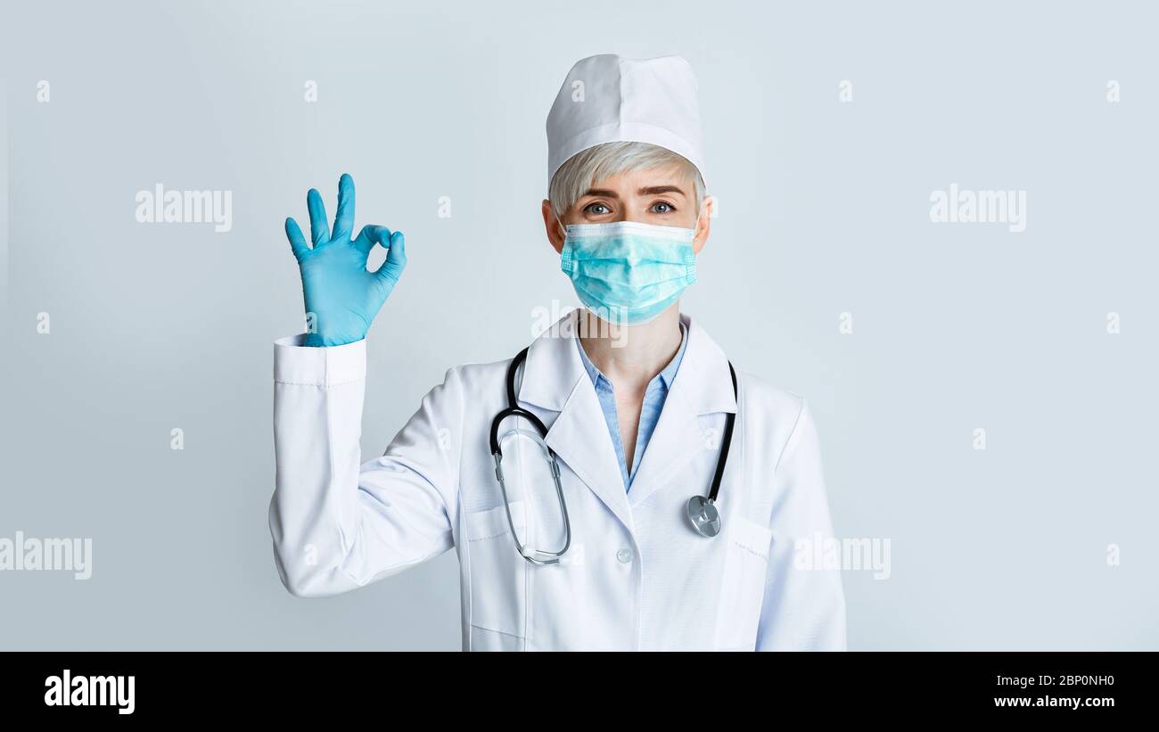 Le médecin affiche le signe ok. Femme en manteau blanc avec masque médical et gants Banque D'Images