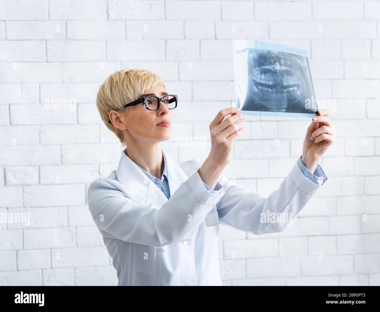 Le médecin regarde les rayons X. Femme dentiste regarde un cliché des dents sur fond de mur de brique blanche Banque D'Images