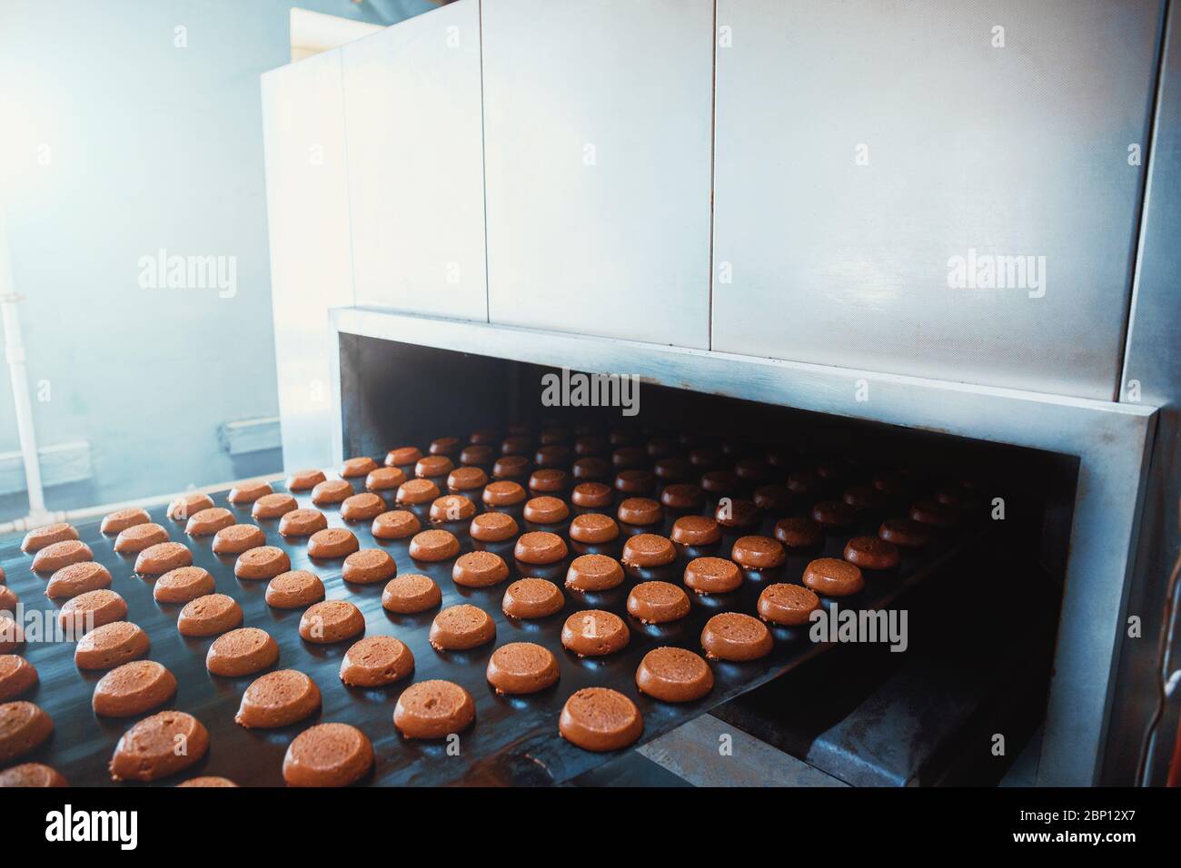 Tapis transporteur automatique avec gâteaux, processus de cuisson dans l'usine de confiserie. Industrie alimentaire, tonifiée Banque D'Images