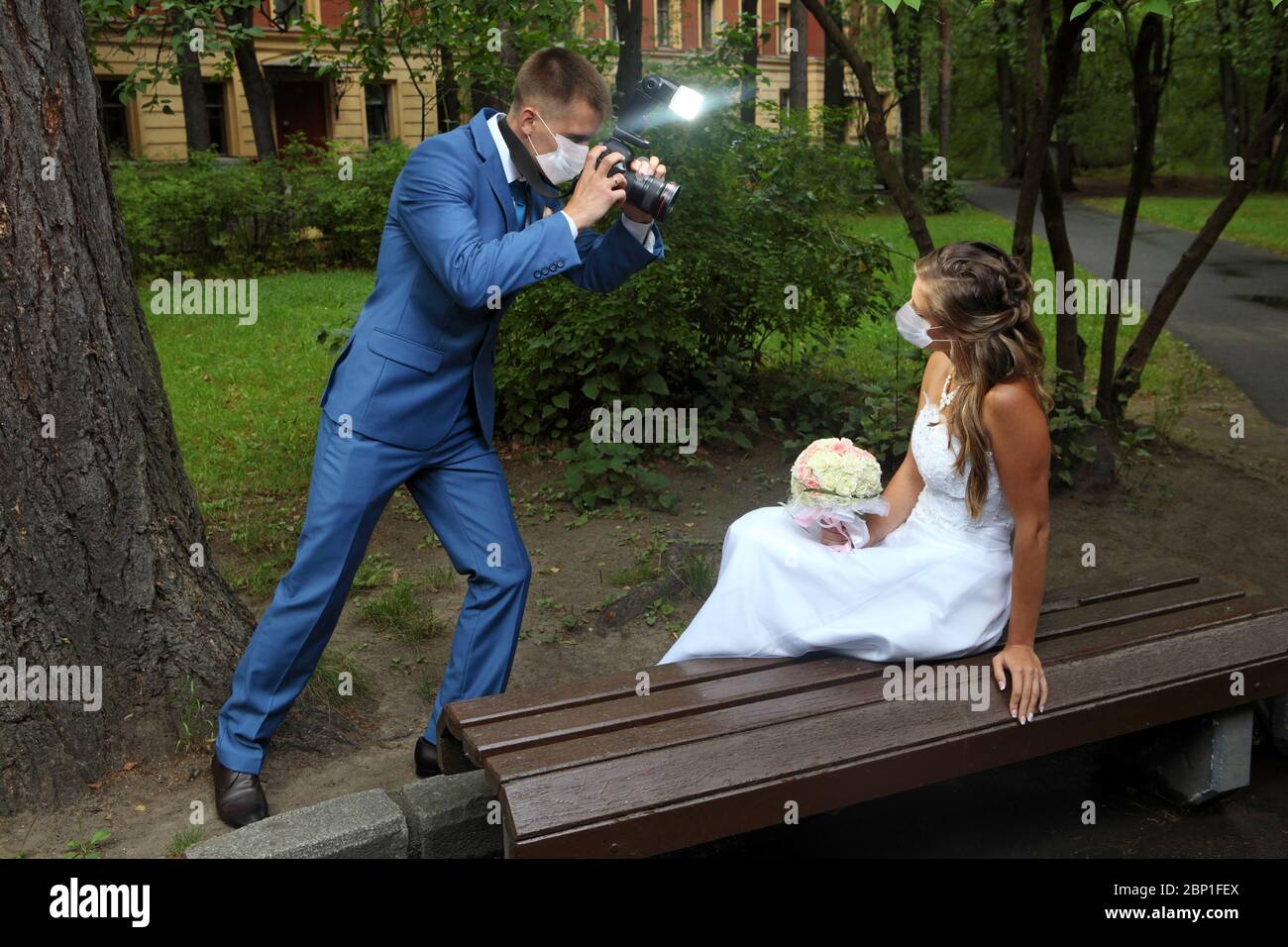 Photographier la mariée et le marié dans le parc, ils portent des masques protecteurs du visage pendant la pandémie d'infection à coronavirus Covid-19, saison de mariage été Banque D'Images