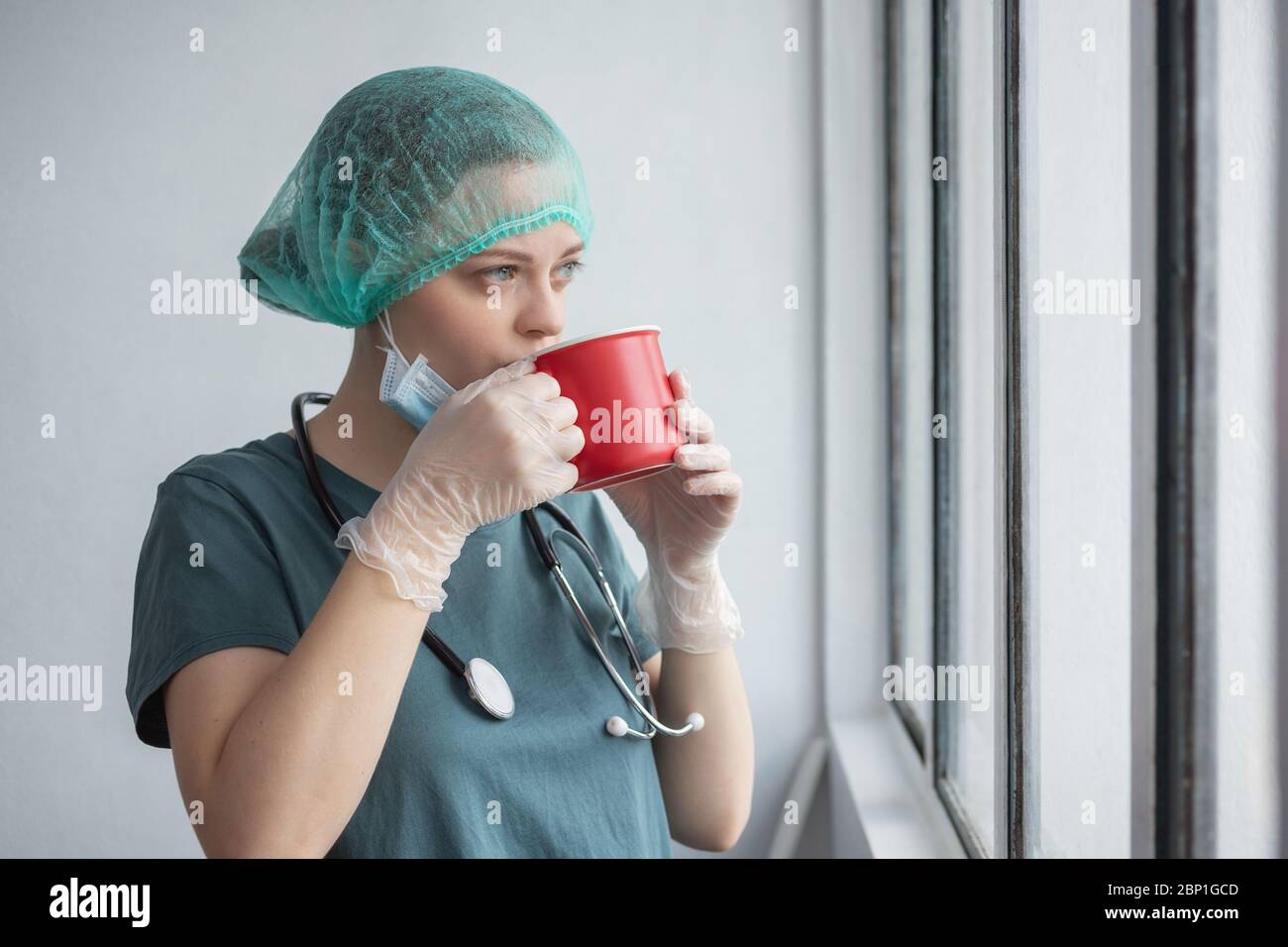 Jeune femme caucasienne médecin infirmière dans le masque chirurgical semble fatigué. Pause-café pendant l'éclosion du coronavirus covid-19 Banque D'Images
