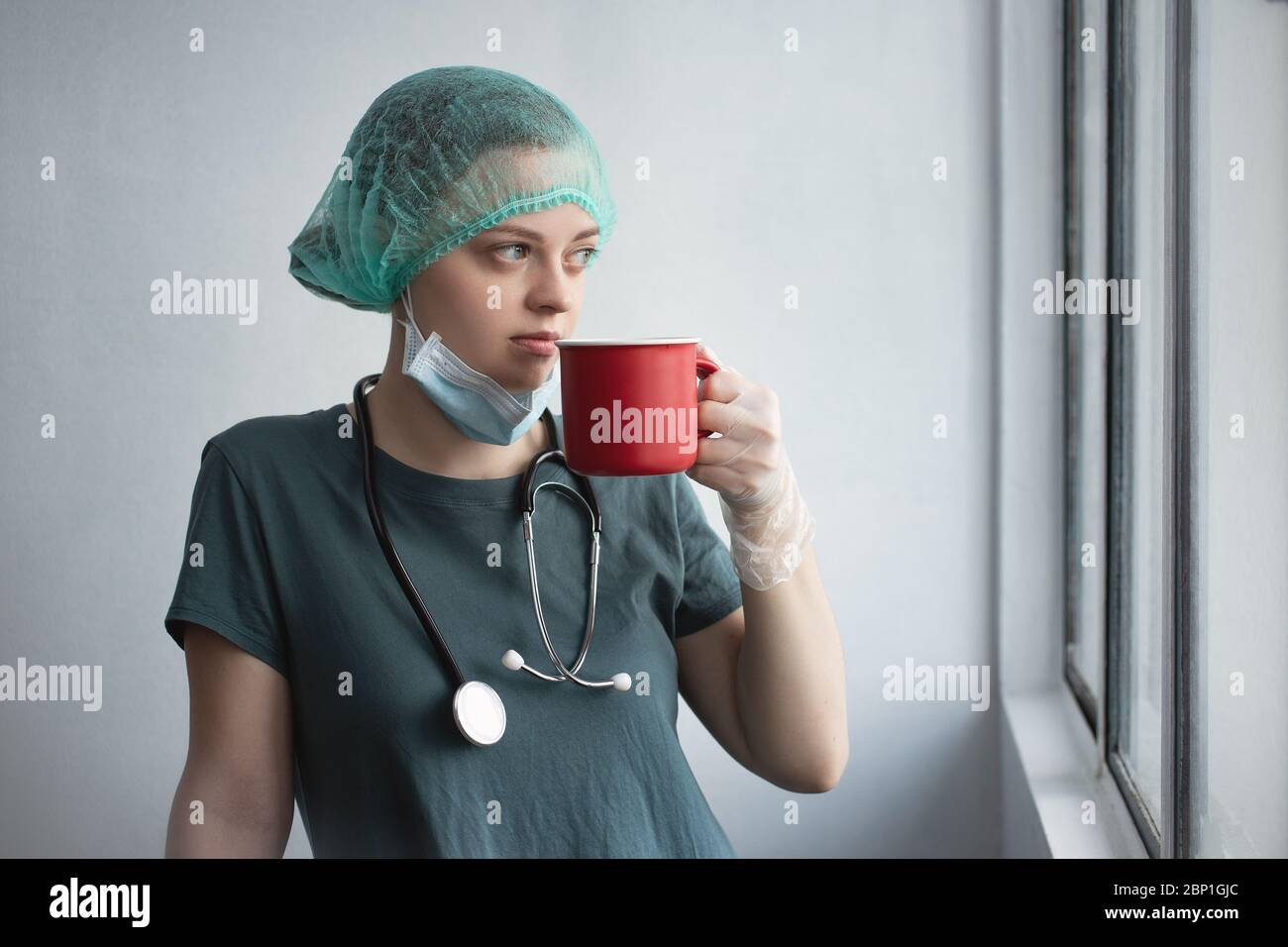 Jeune femme caucasienne médecin infirmière dans le masque chirurgical semble fatigué. Pause-café pendant l'éclosion du coronavirus covid-19 Banque D'Images
