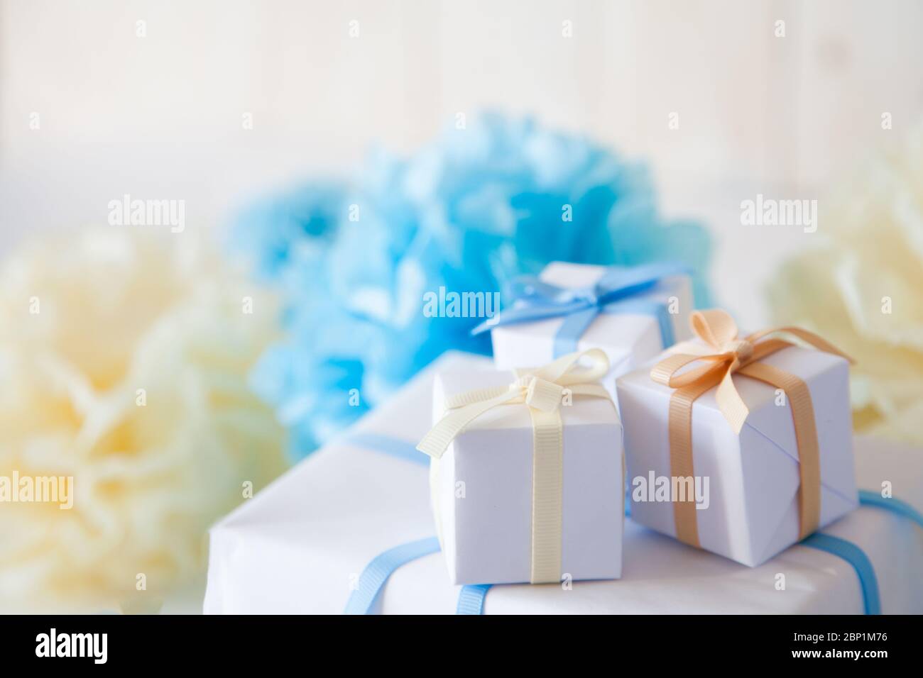 Boîte cadeau blanche avec rubans bleus, jaunes et beiges sur fond blanc. Banque D'Images