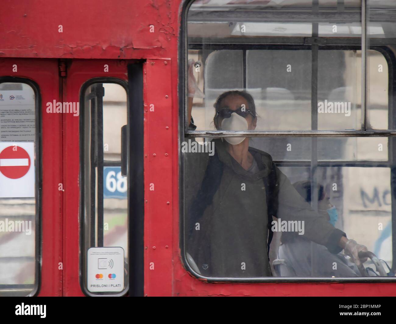 Belgrade, Serbie - 15 mai 2020 : femme portant un masque chirurgical tout en prenant un tramway rouge, de l'extérieur Banque D'Images