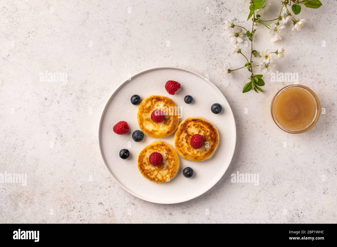 Cheesecake russe traditionnel avec framboises, bleuets et miel sur une plaque en céramique blanche sur fond clair. À côté de lui est une branche de floraison Banque D'Images