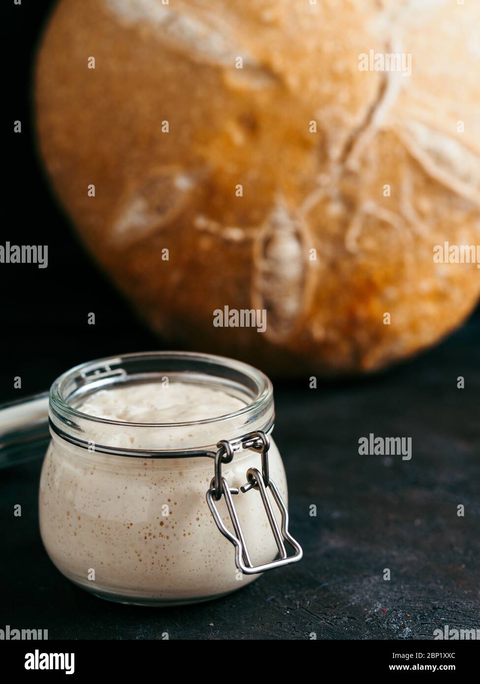 Pain de base Sourdoug et pain de levain de blé. Entrée de pâte aigre de blé dans un pot en verre et délicieux pain de pâte à pain rond maison sur fond noir. Concept de fabrication de pain au levain fait maison. Verticale Banque D'Images