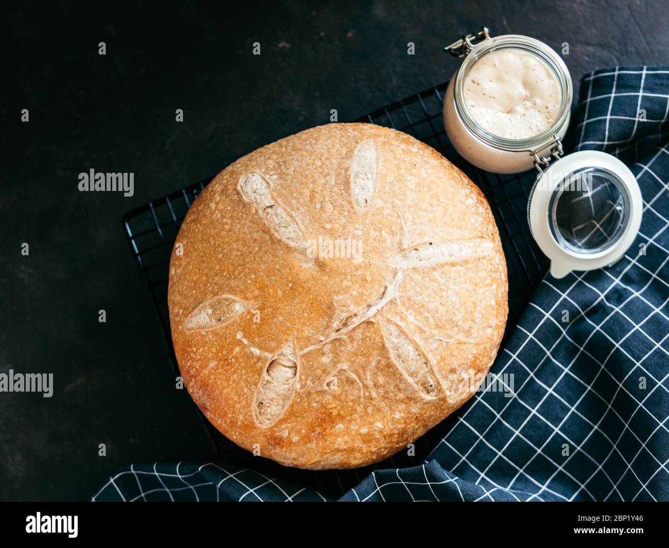 Pain au levain rond de blé et entrée de levain dans un pot en verre. Vue de dessus de délicieux pain de levain maison sur fond noir avec espace de copie. Concept de fabrication de pain au levain fait maison. Banque D'Images