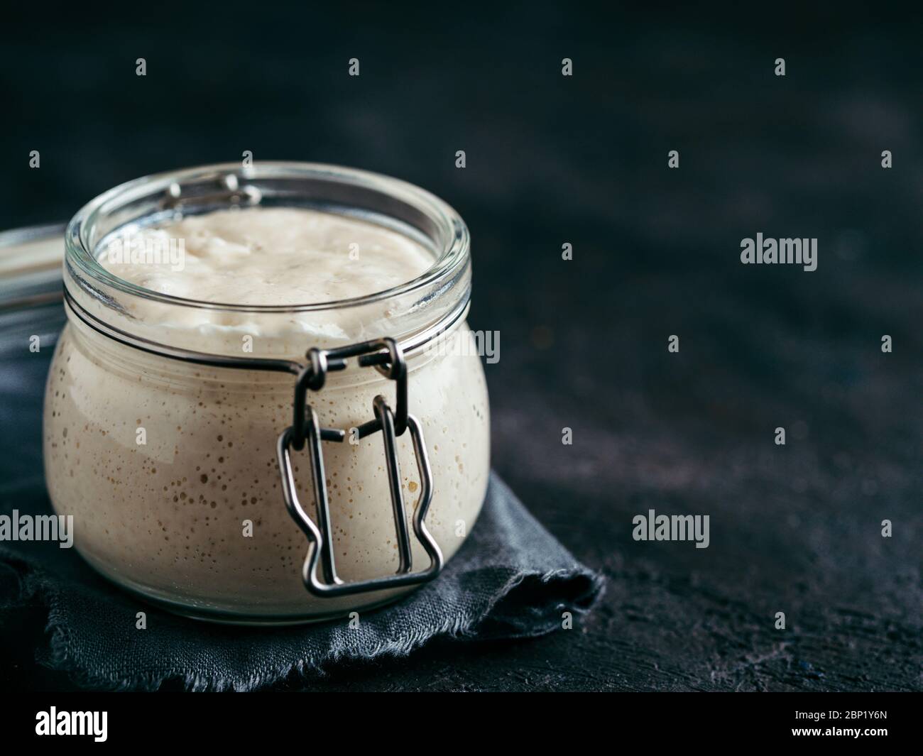 Démarreur de levain de blé. Bol en verre avec entrée de levain sur fond sombre, espace de copie. Banque D'Images