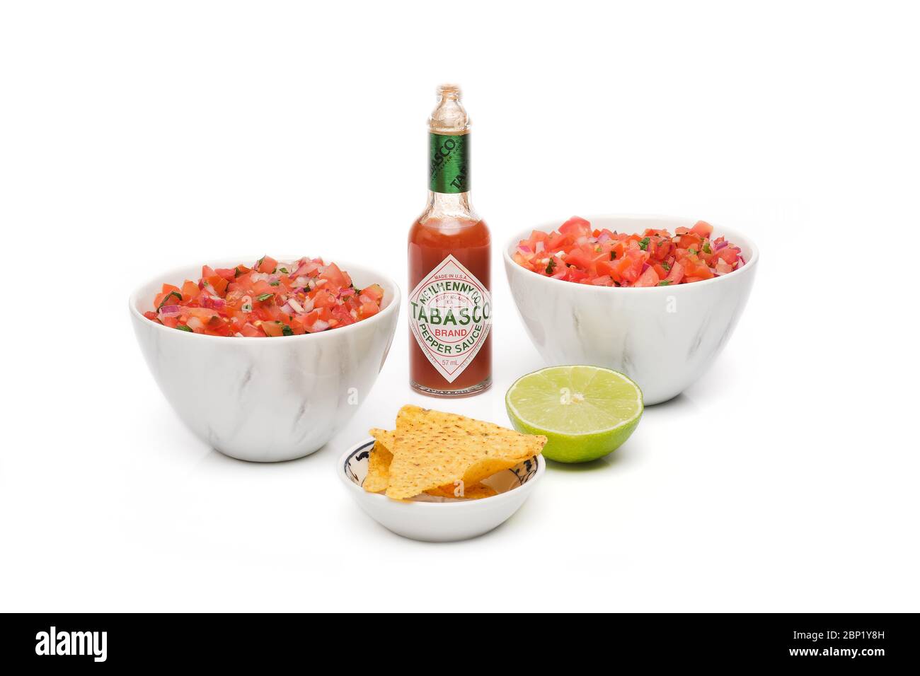 2 bols identiques contenant de la salsa fraîchement préparée avec une bouteille de sauce tabasco, un bol de chips tortilla et une demi-tranche de lime fraîche Banque D'Images