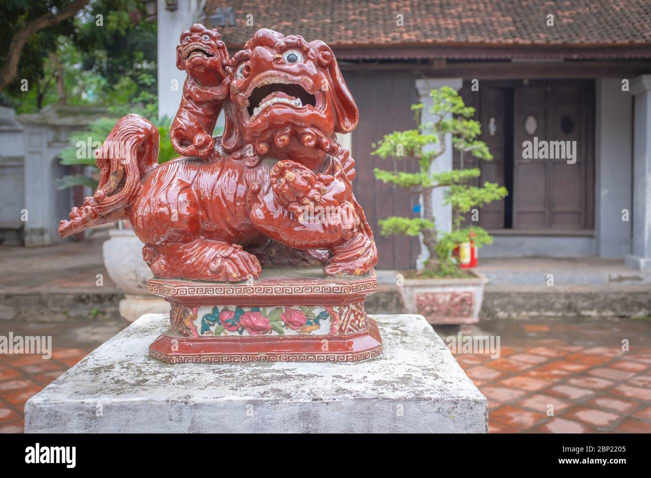 Lion asiatique traditionnel en porcelaine rouge, pris dans un parc de la ville avec des bonsaïs en arrière-plan, Hanoi, Vietnam Banque D'Images