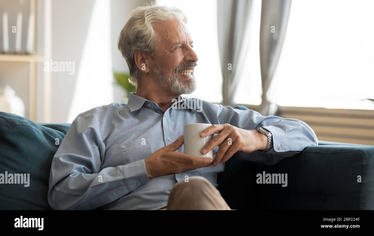 Joyeux homme âgé reposant sur un canapé avec une tasse de thé. Banque D'Images