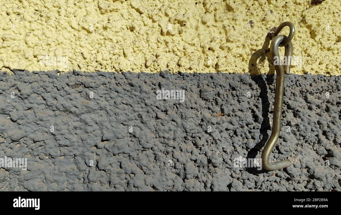 Crochet métallique rouillé de loquet obsolète accroché sur un fond de mur rugueux de bandes jaunes et grises. Texture de mur de plâtre inégal et de vieille moraillon Banque D'Images