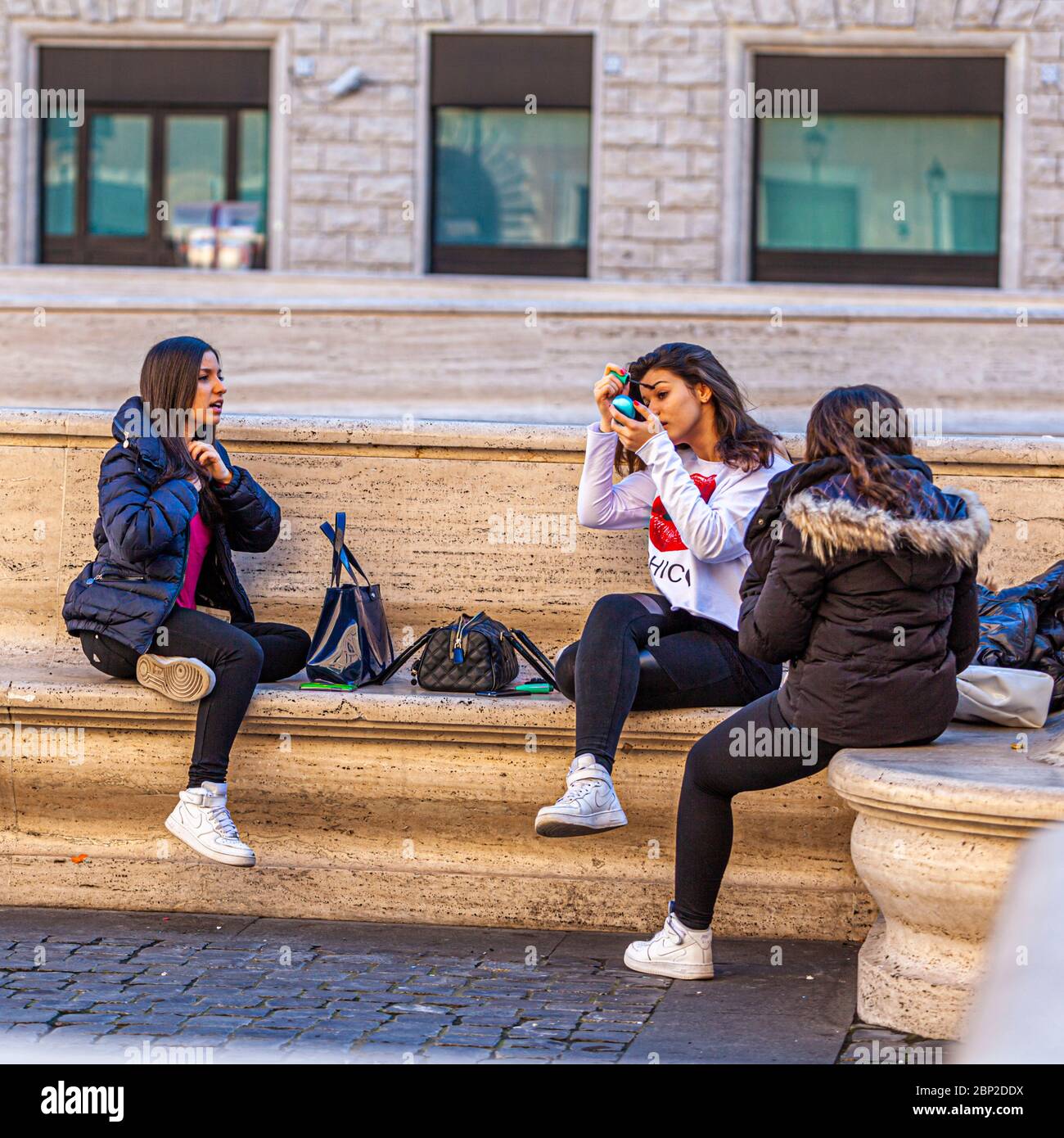 Trois filles appliquant des cosmétiques sur un banc public à Rome, Italie Banque D'Images