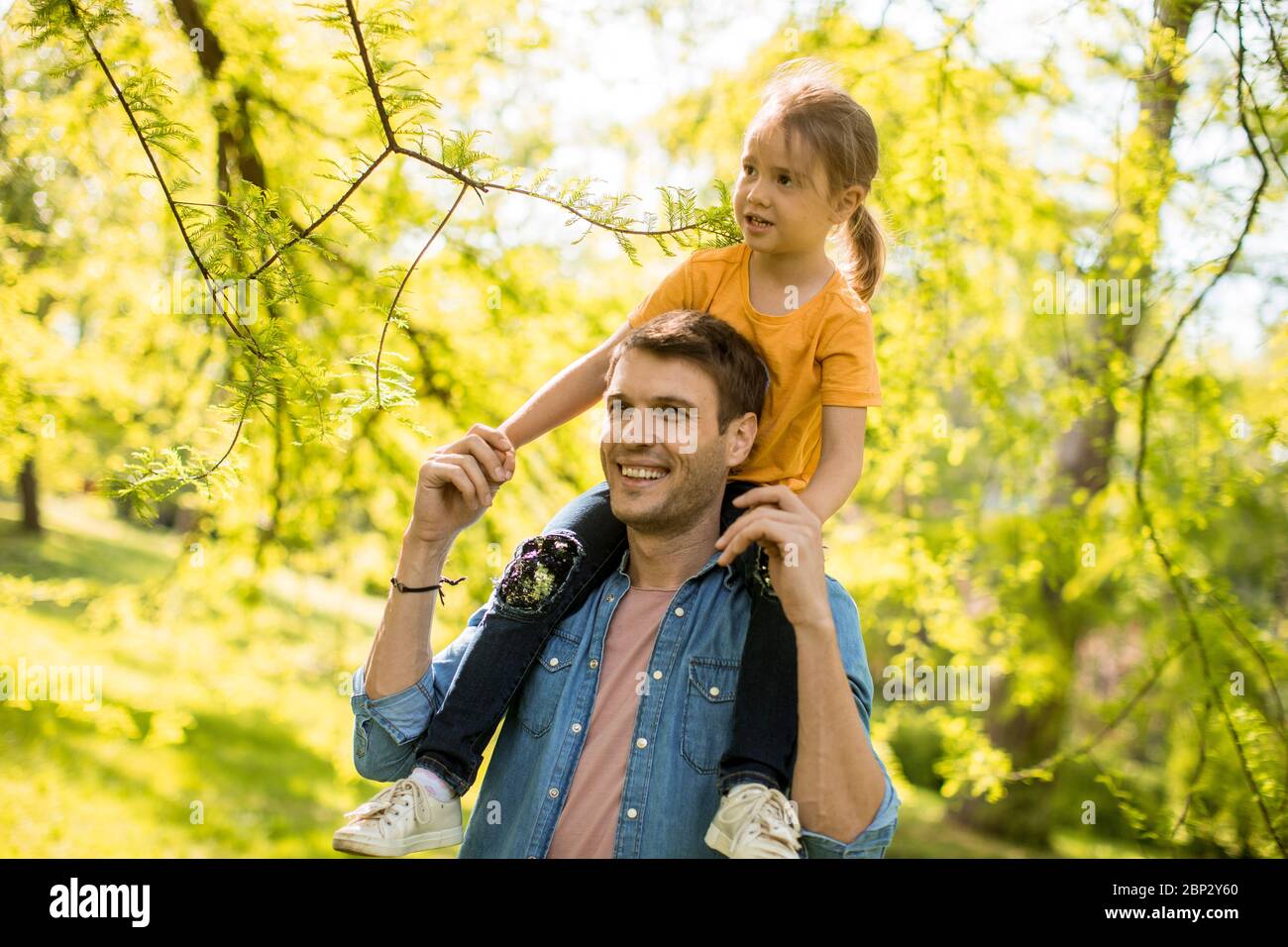 Petite fille mignonne assise sur les épaules du père dans le parc par une journée ensoleillée Banque D'Images