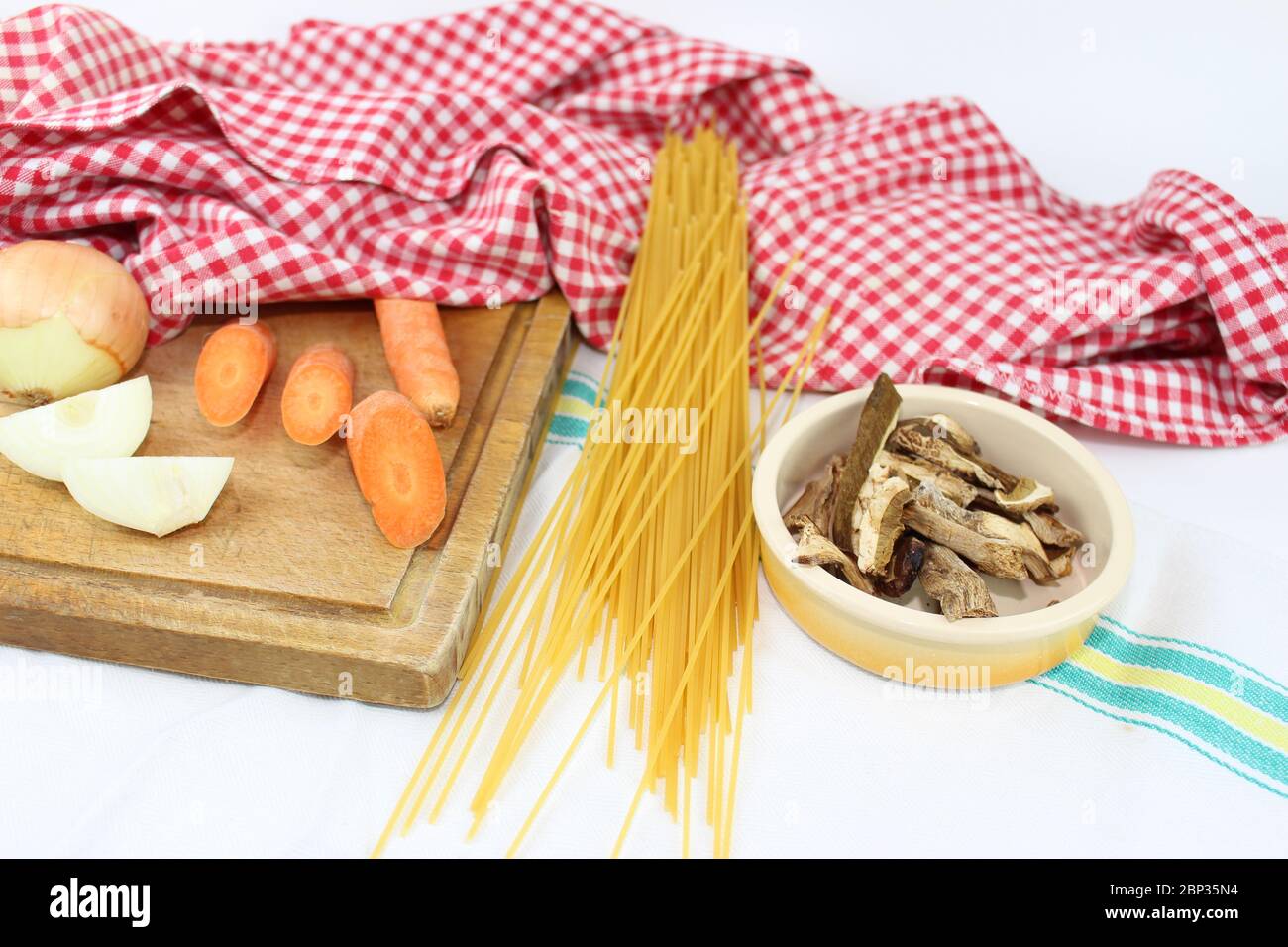 Produits alimentaires disposés sur la table à volants, avec des carrés rouges et blancs. Cuisine méditerranéenne italienne avec spaghetti et champignons porcini séchés. Banque D'Images