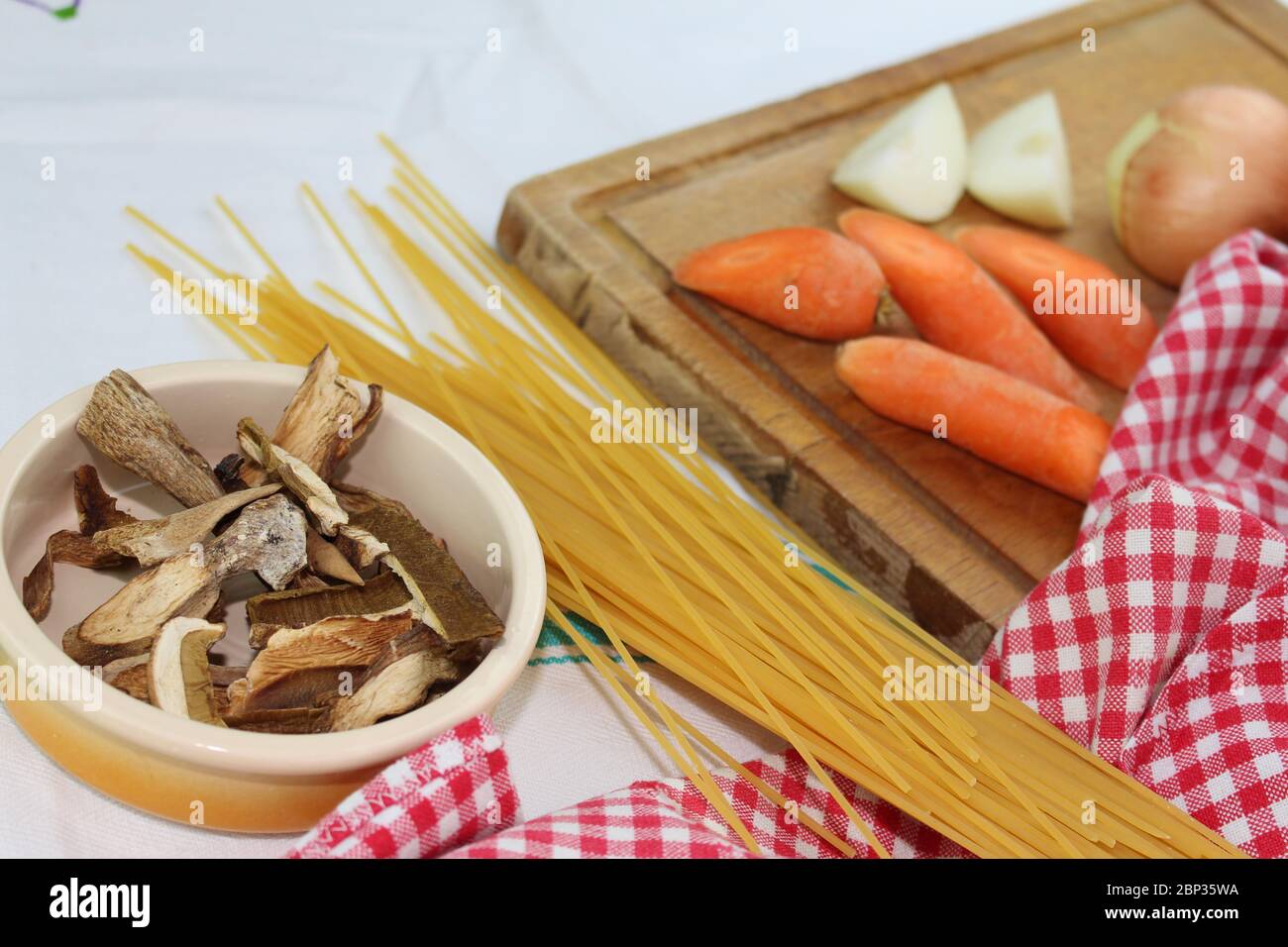 Produits alimentaires disposés sur la table à volants, avec des carrés rouges et blancs. Cuisine méditerranéenne italienne avec spaghetti et champignons porcini séchés. Banque D'Images