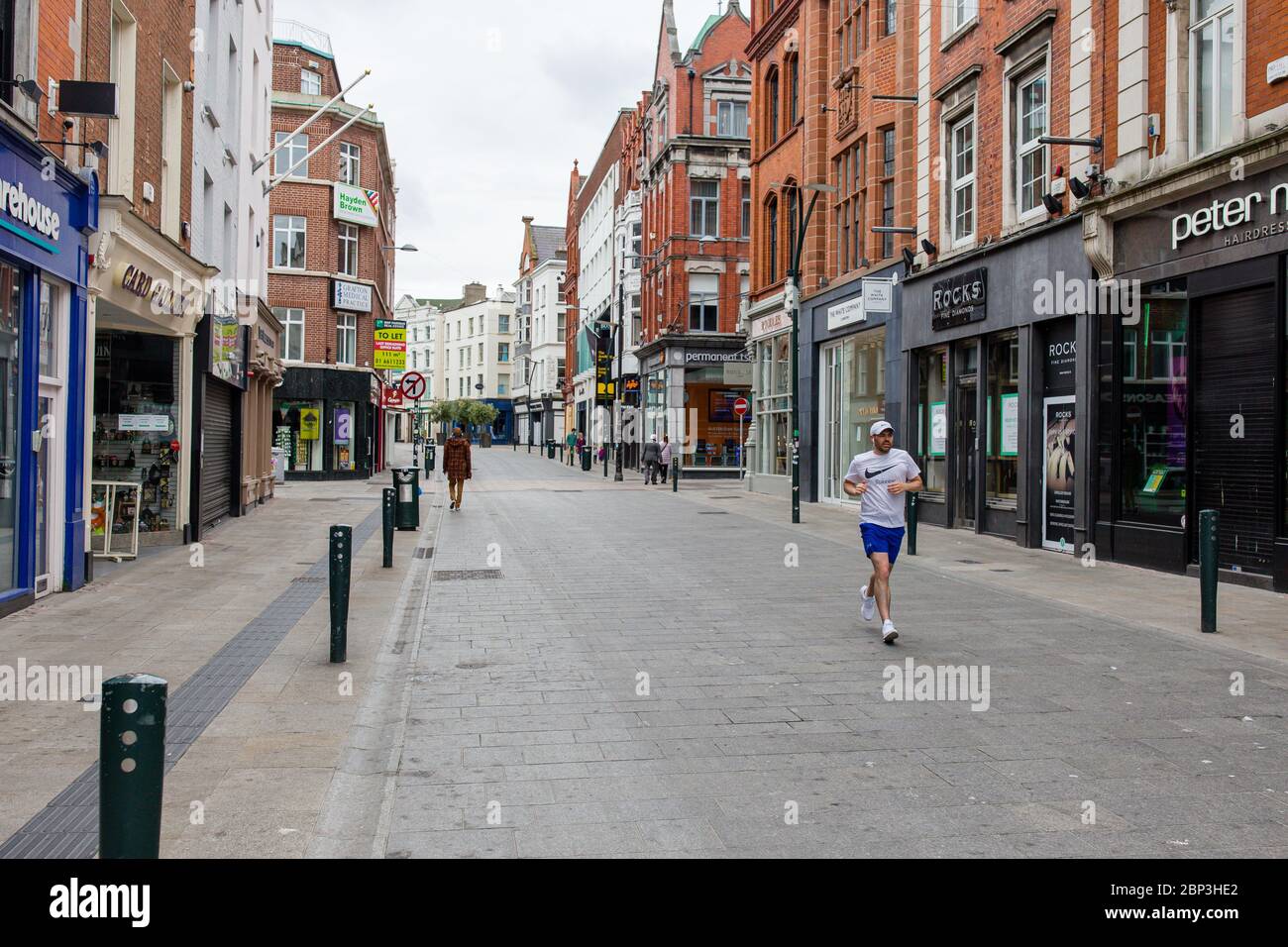 Des piétons se balader dans une rue Grafton déserte du centre-ville de Dublin alors que les magasins restent fermés en raison de restrictions liées à une pandémie de coronavirus. Banque D'Images