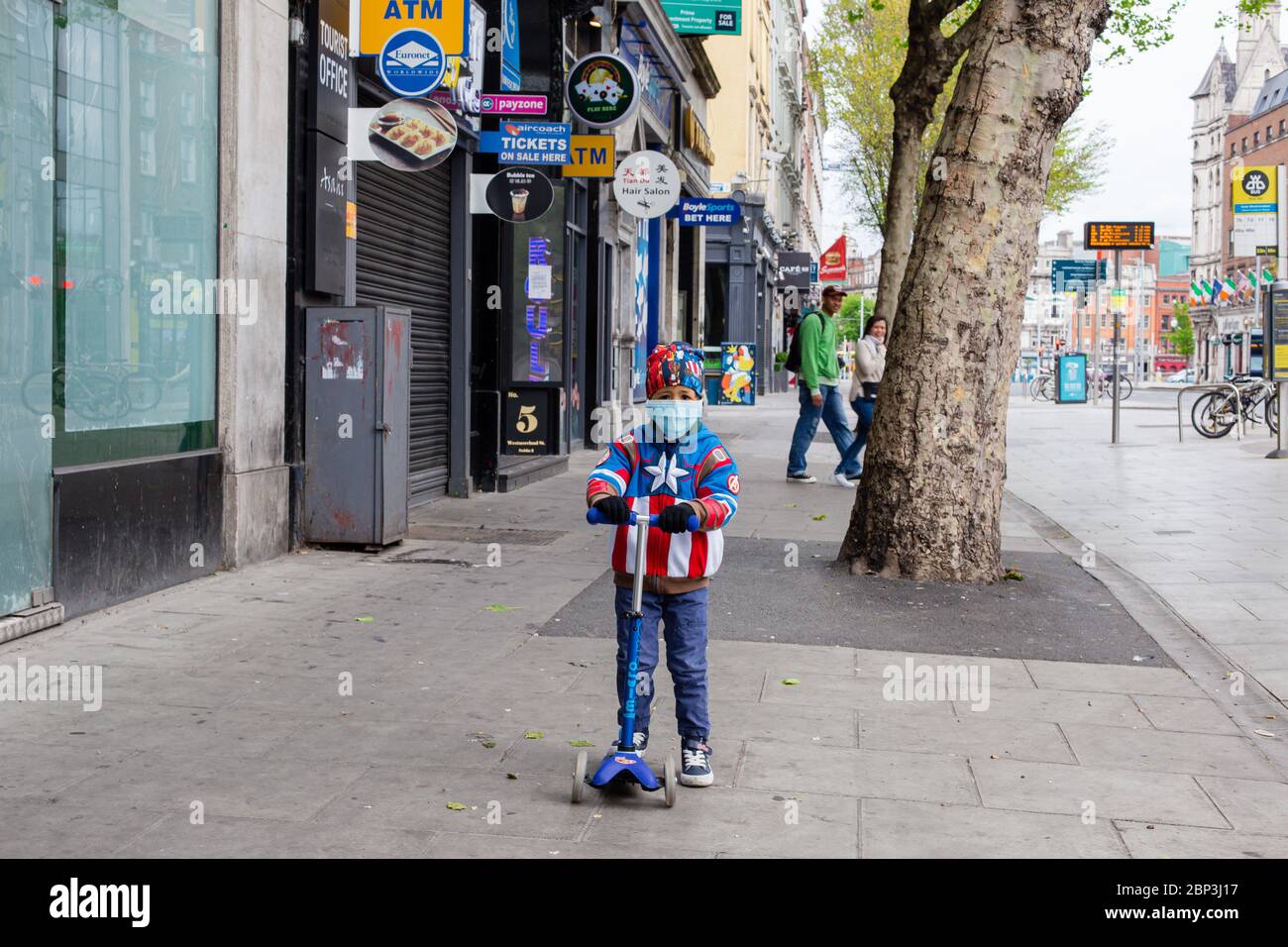 Garçon sur un scooter portant une veste superhéros et un masque facial protecteur qui se frayait à travers le Str Westmoreland déserté à Dublin pendant la pandémie de Covid-19 Banque D'Images
