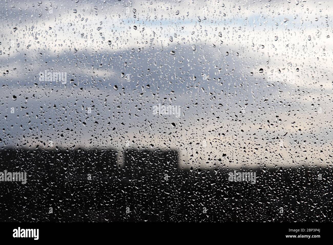 Gouttes de pluie sur la vitre sur fond flou de ciel nuageux. De belles gouttes d'eau, temps pluvieux en ville Banque D'Images