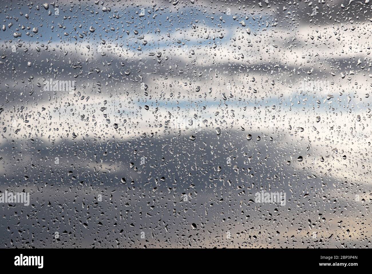 Gouttes de pluie sur la vitre sur fond flou de ciel nuageux. De belles gouttes d'eau, temps pluvieux en ville Banque D'Images